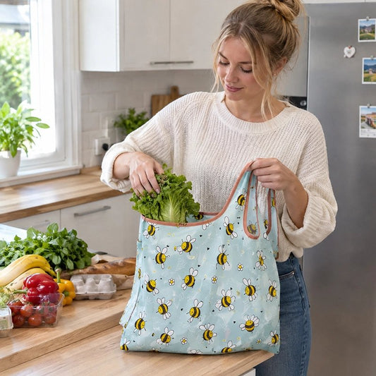 jeune-femme-blonde-souriante-vetue-dun-pull-blanc-et-un-jeans-bleu-range-une-salade-verte-dans-un-sac-reutilisable-bleu-ciel-decorer-de-petites-abeilles-jaunes-et-noires-sur-le-comptoir-dune-cuisine-moderne-et-lumineuse