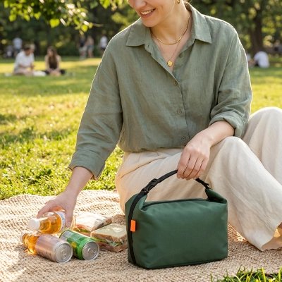 une-femme-profite-dun-pique-nique-dans-un-parc-accompagner-dun-petit-sac-isotherme-vert-foncer-rectangulaire-muni-dune-poigner-noir-pour-un-transport-facile