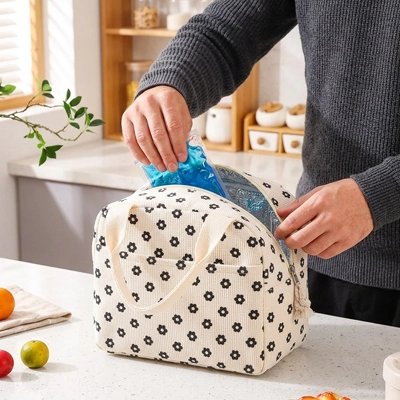 une-personne-glisse-un-bloc-refrigirant-bleu-dans-un-sac isotherme-blanc-a-motifs-floraux-noirs-compact-et-pratique-il-est-ideal-pour-conserver-les-repas-et-boissons-au-frais-lors-des-deplacements